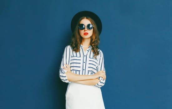 Fashion pretty woman wearing a black sunglasses, hat and white skirt posing over a gray background