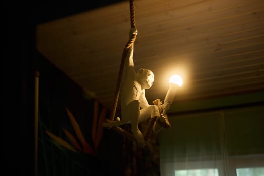 A playful monkey figurine swings from a stylish light fixture, casting a warm glow in a cozy living space