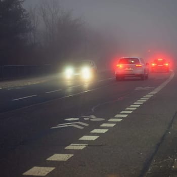 Bright headlights of a car driving on foggy winter road