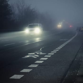 Bright headlights of a car driving on foggy winter road