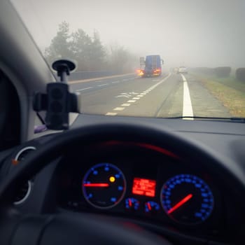 Car traveling on the foggy road with headlights or headlamps on. Low visibility - Dangerous driving of cars in winter in bad weather
