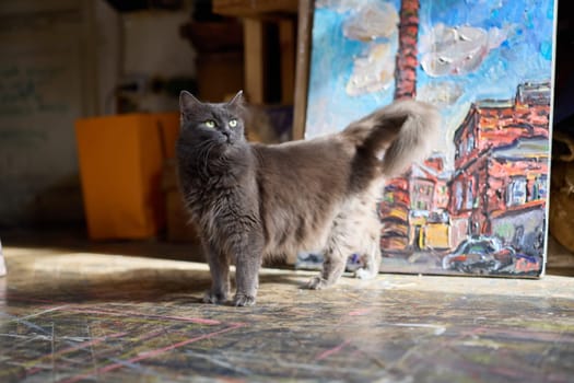 A playful gray cat stands proudly in a vibrant art studio filled with stunning artworks and a creative vibe