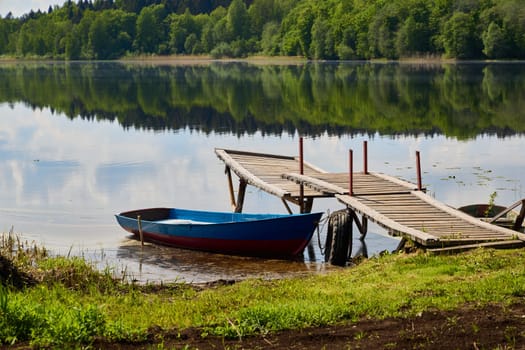 A wonderful and serene lakeside view featuring a wooden dock alongside a vibrant boat reflecting in calm waters