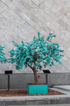 A captivating turquoise tree sculpture with vibrant accents, beautifully showcased against a sleek modern wall