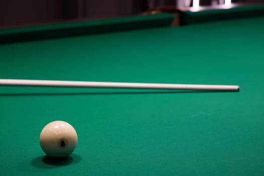 Closeup of a pristine white ball, elegant cue stick, and vibrant green felt pool table, capturing billiards