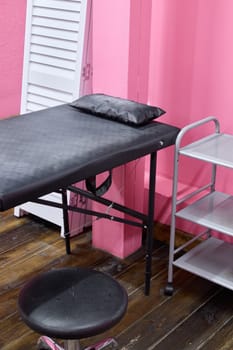 In this stylish minimalist treatment room, there is a sleek black examination table along with modern shelving units