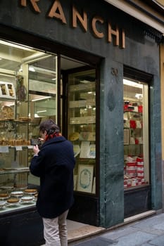 Cremona, Italy - November 20th 2024 Tourist taking pictures of a traditional pastry shop window displaying various desserts and awards in cremona, italy