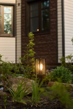 A cozy garden lantern gently glowing softly beside a stylish modern home surrounded by lush, vibrant greenery