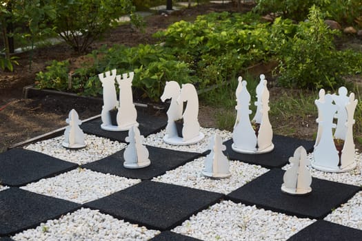 A striking outdoor chess set that features large, elegant white pieces, set against a beautiful garden backdrop