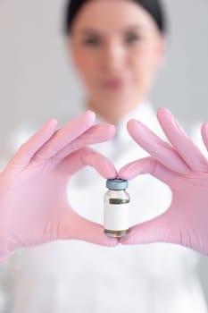 Anonymous female dermatologist holding medicine bottle with blank space for injection in clinic. Young cosmetology therapist is wearing pink gloves in beauty spa salon.