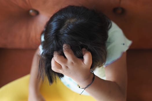 A young child is seated thoughtfully, with a hand resting on their head, deeply lost in thought