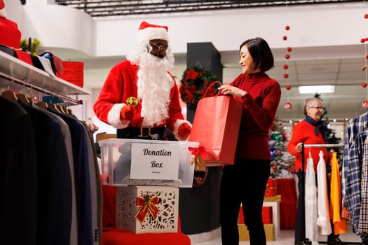People putting clothes in donation box with santa claus employee, donating things for poor children. Diverse clients gathering clothing to donate to charity for christmas holiday.