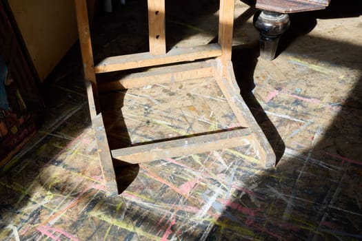 A rustic wooden chair casts a shadow on a colorful art studio floor, showcasing creativity and inspiration