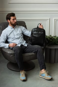A man is comfortably seated in a chair with a backpack resting beside him, creating a relaxed and casual atmosphere around him