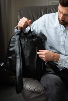 A man is comfortably seated in a chair with a backpack resting beside him, creating a relaxed and casual atmosphere around him