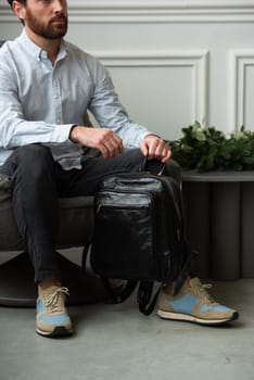 A man is comfortably seated in a chair with a backpack resting beside him, creating a relaxed and casual atmosphere around him