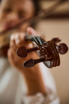 A focused view of a musician's hand adjusting the tuning pegs of a violin. The soft background highlights the intricate details of the instrument and evokes a sense of passion and artistry.
