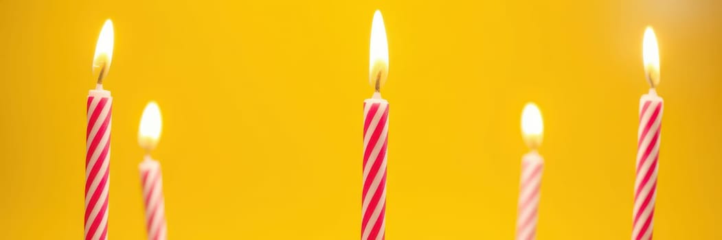 Four brightly striped birthday candles burn gently against a vibrant yellow backdrop, enhancing the joyful ambiance of a birthday celebration. The warm flames add to the festive spirit.