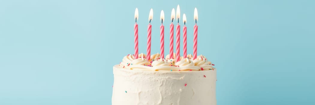 A white frosted birthday cake sits on display featuring pink striped candles, colorful sprinkles, and a vibrant blue backdrop, perfect for a festive celebration.