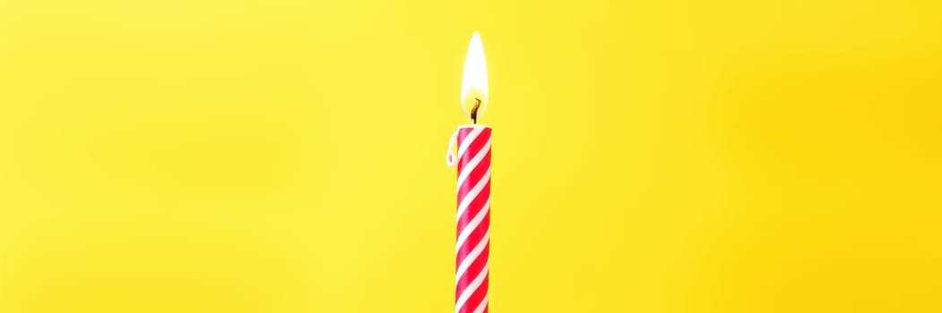 A bright red and white striped birthday candle burns steadily, casting a warm glow against a vibrant yellow background, perfect for a joyful celebration.