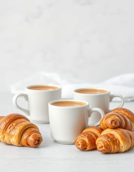 Three white cups filled with rich coffee are arranged beside delicious, flaky croissants on a light-colored table. The scene is bright and inviting, perfect for a morning indulgence.