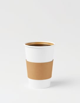 A white coffee cup with a cardboard sleeve is filled with a warm drink. Its simple design emphasizes the rich color of the beverage, set against a neutral backdrop.