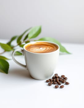 A white cup holds a perfectly crafted latte topped with intricate foam art, placed beside roasted coffee beans and fresh green leaves on a minimalist countertop.