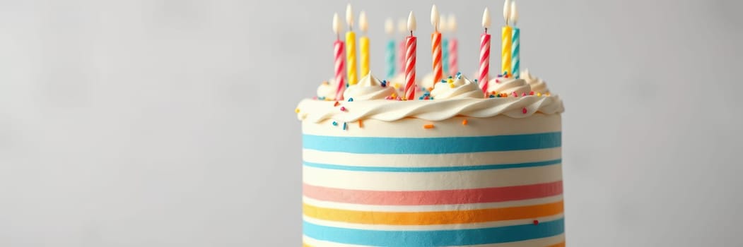 A festive cake featuring bright stripes and topped with lit candles. It serves as a centerpiece for a birthday celebration, conveying joy and anticipation.