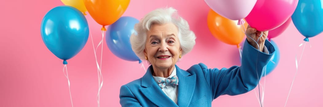 An elderly woman in a blue suit joyfully holds multiple vibrant balloons, smiling brightly in front of a pink background, embodying the spirit of a festive celebration.