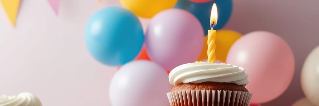 A festive birthday setup features a cupcake topped with a lit candle, surrounded by vibrant balloons in various colors, suggesting a cheerful celebration moment.