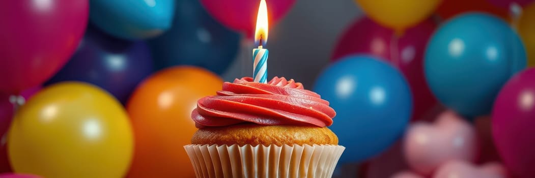 A delicious cupcake topped with pink frosting and a blue candle stands out, surrounded by bright, colorful balloons hinting at a joyful birthday celebration.
