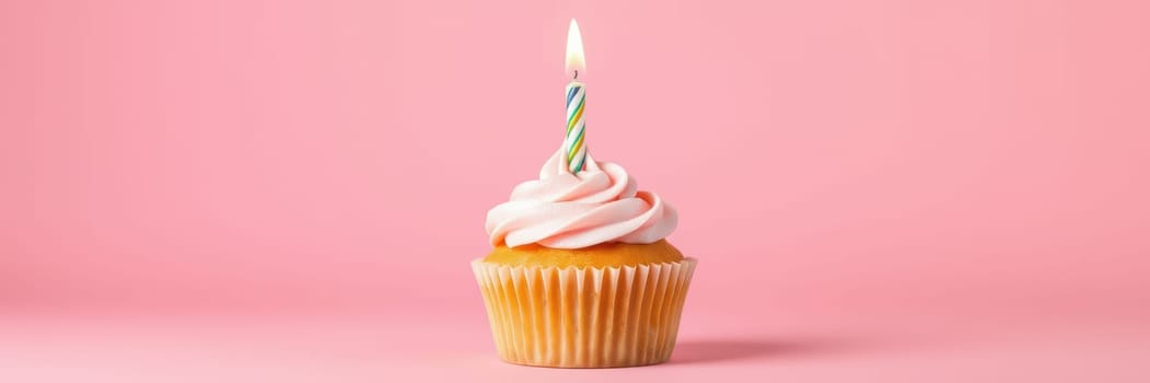 A vibrant cupcake sits on a light pink surface, topped with swirls of soft pink frosting and a colorful candle, perfect for a birthday celebration or sweet occasion.