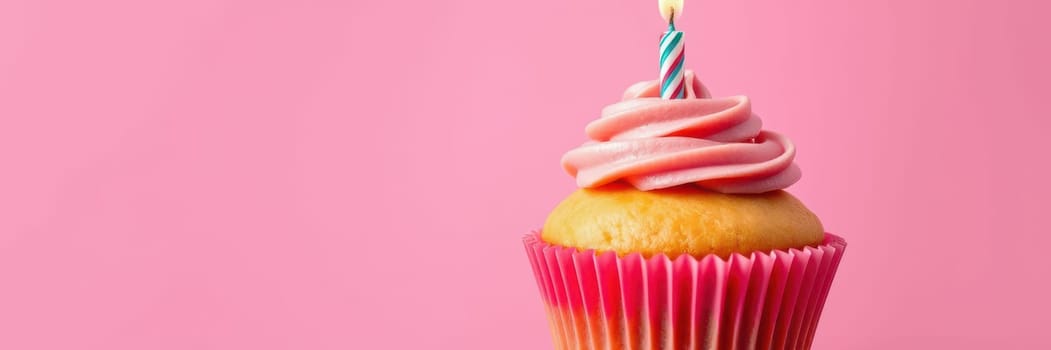 A beautifully decorated cupcake topped with swirls of pink frosting and a lit candle sits prominently against a bright pink background. Perfect for any festive occasion.