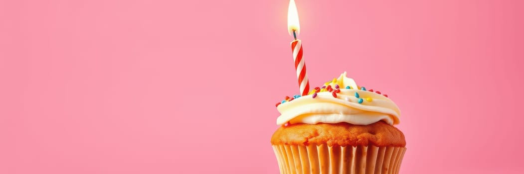 A delightful cupcake topped with creamy frosting and colorful sprinkles features a lit candle on a vibrant pink backdrop, creating a festive atmosphere for celebration.