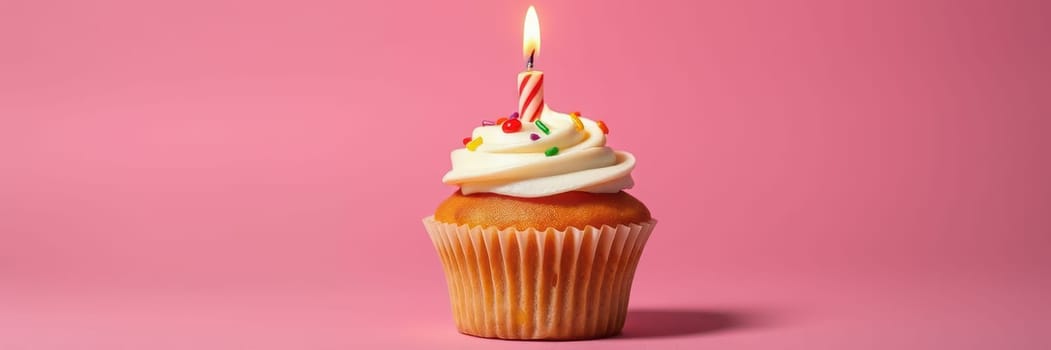 A delicious cupcake topped with white frosting and colorful sprinkles sits proudly against a vibrant pink backdrop, with a lit candle ready for celebration.