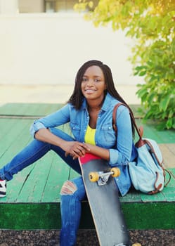 Portrait of happy smiling young african woman model posing with skateboard in the city