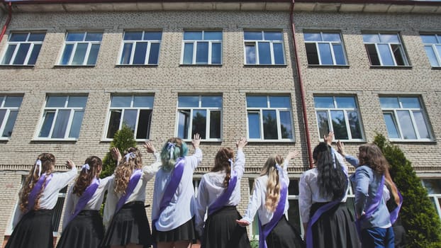 Group of graduating students waving goodbye to their school building on their last day, celebrating the end of an era and the start of a new chapter