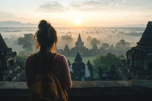 A young woman stands in silhouette, admiring a breathtaking sunrise over an ancient temple complex shrouded in mist, evoking a sense of tranquility and adventure.