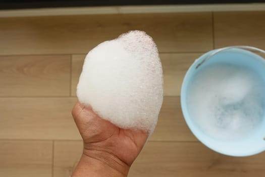 A hand firmly grasping a fluffy and abundant handful of white soapy foam inside a bucket