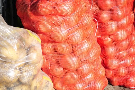 A variety of fresh bags filled with red onions, potatoes, and assorted vegetables are stacked