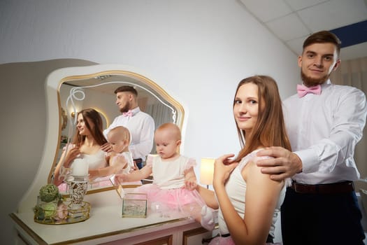 A smiling couple poses with their baby girl at a charming vanity, showcasing joy and affection in a warm and stylish setting.