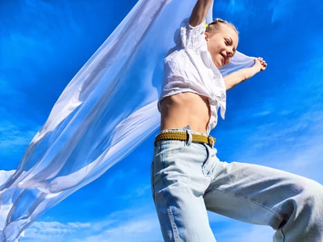 A young woman expresses happiness while dancing with a light scarf in the bright sunlight on a clear day.