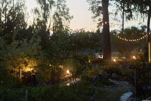 A tranquil evening garden scene, beautifully illuminated by soft lights and lovingly surrounded by natures beauty