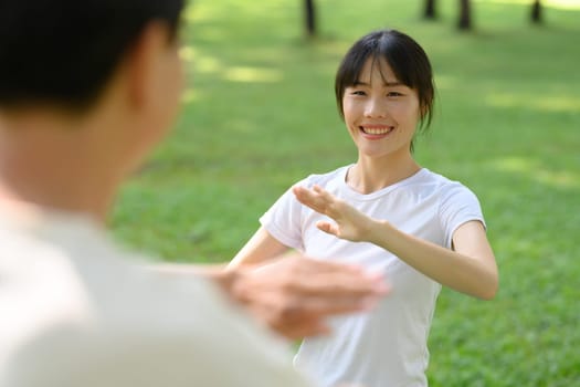Cheerful asian woman and father practicing Tai Chi in the park. Healthy and outdoor activity concept.