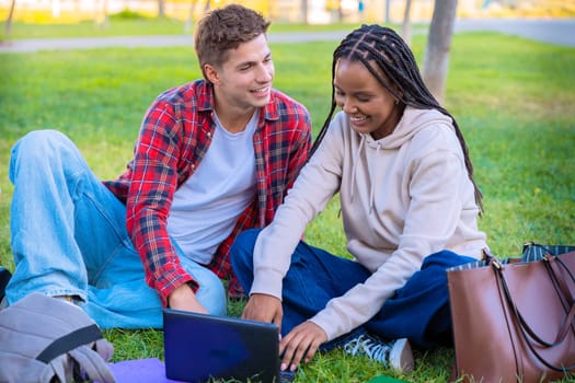 Young A young couple sits together on the grass outdoors, smiling and using a laptop. They are relaxed and enjoying their time, with bags and books around them, in a calm and bright natural setting.