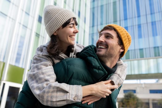 Young couple laughing and enjoying piggyback ride in city during winter vacation