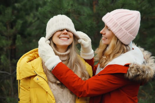 Happy smiling women friends having fun, celebration, joyful girlfriends together on Christmas tree background in winter forest, wearing hat, colorful jacket outdoors