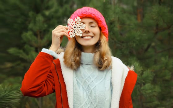 Winter day, happy smiling young woman with snowflakes decoration toys having fun enjoys snow, warm weather against Christmas tree, joyful girl in hat standing in snowy forest
