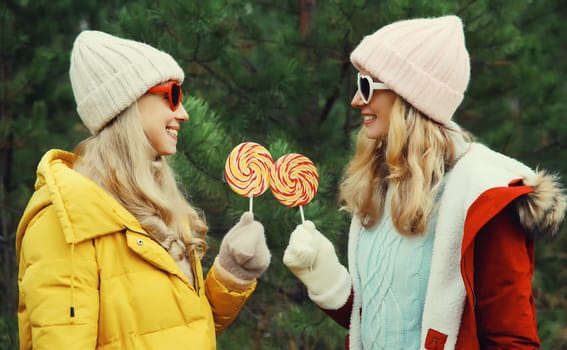 Happy smiling women friends having fun, celebration, joyful girlfriends together on Christmas tree background in winter forest, wearing hat, colorful jacket outdoors