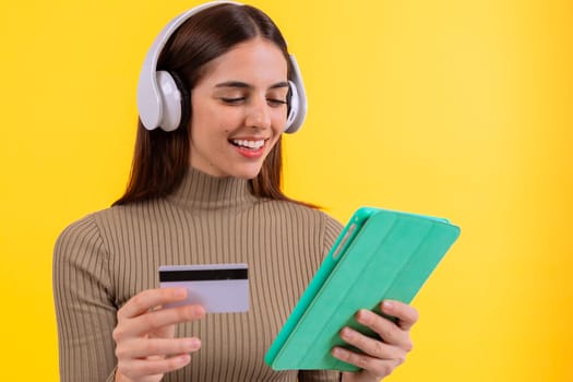 A woman smiles while holding a tablet and a credit card in front of a bright yellow background. His joyful expression creates a positive and engaging atmosphere.
